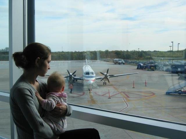 žena s dítětem v náručí u okénka v letištní hale